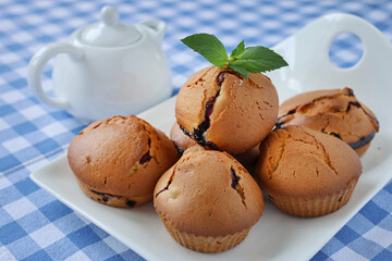 Blueberry muffins in a white plate on a table with a blue tablecloth decorated with mint