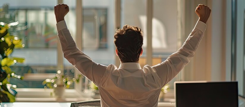 Joyful man in office with raised hands celebrates happily copy space image