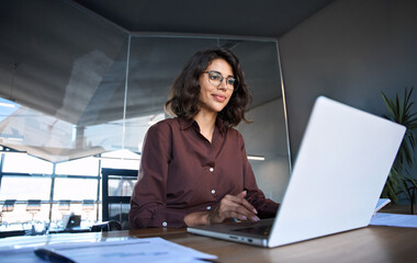 Young professional it specialist latin hispanic business lady working on laptop pc sitting at desk...
