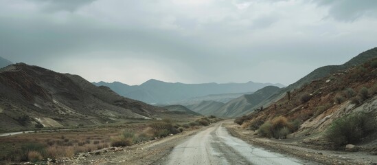 Mountainous landscape with a gray overcast sky stretching above it An empty road meanders through the hilly terrain with a blurred background and a focus on copy space image