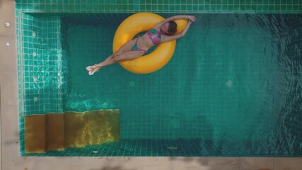 Young woman is enjoying her vacation, floating on yellow inflatable ring in swimming pool. Concept of summer vacation, relaxing in resort