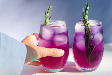 An unrecognizable female hand takes a purple cocktail from the table.