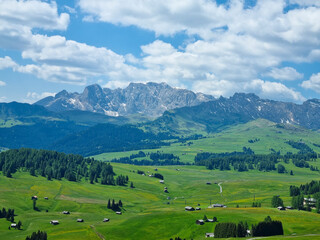 There are tiny roads and houses in a wide field with a clear view, and stone mountain peaks beyond.