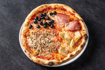 Italian four seasons pizza with tomato, mozzarella, cooked ham and mushrooms, isolated on black marble table background