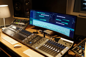 Professional recording studio featuring mixing consoles, monitor speakers, and computer displaying audio editing software. Spacious desk creating environment suitable for sound engineering