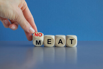 Man turns a wooden cube and form the expression 'eat no meat'. Beautiful grey table blue background