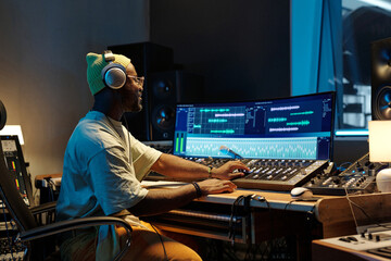 Person wearing headphones working on audio editing in modern studio with professional equipment on desk and screen displaying sound waveforms