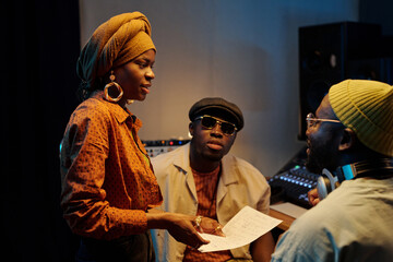 Group of African American artists collaborating in recording studio, analyzing lyrics and sharing ideas while creating music