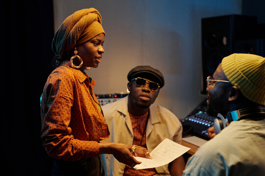 Group of African American artists collaborating in recording studio, analyzing lyrics and sharing ideas while creating music