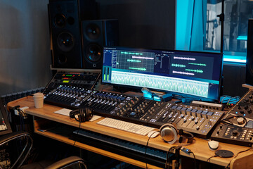 Obraz premium View of professional recording studio with various audio mixing consoles, headphones, and computer screens displaying audio tracks, blue accent lighting illuminating studio space