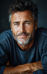 Fototapeta premium A man with a beard and gray hair is smiling at the camera. He is wearing a blue shirt and he is in a relaxed and confident mood