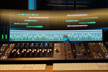 Professional mixing console in recording studio with large monitor displaying multiple sound...