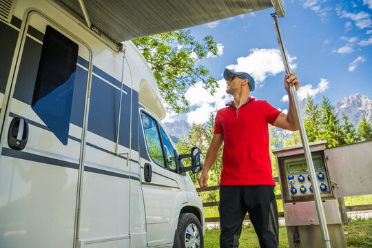 Man Setting up an Awning on an RV Camper Van in a Scenic Campground During the Day