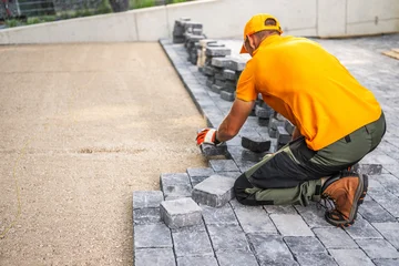 Fotobehang Oranje Worker Laying Cobblestones for a Patio in a Residential Backyard on a Sunny Day  © Tomasz Zajda