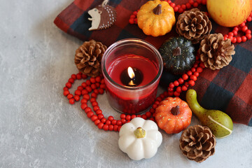 Pumpkin, fir cones, red rosary made of Rowan berries, burning candle and  warm red and grey plaid. Autumn mood still life. 