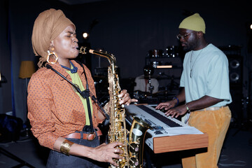 Musicians collaborating in recording studio. One playing saxophone while other playing keyboard....