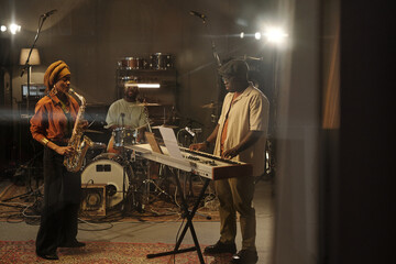 Musicians jamming in studio with saxophonist, drummer, and keyboardist engaged in passionate...