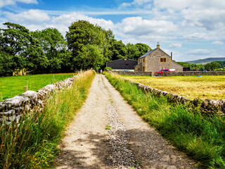Quaint stone farmhouse along a picturesque gravel road framed by lush greenery and pastures under a...