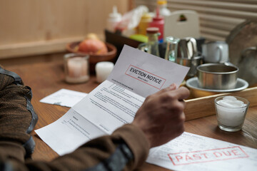 Person holding eviction notice at wooden table with various condiments and utensils scattered...