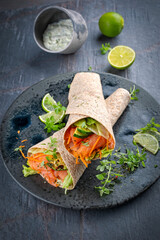 Italian style wrap piada tortilla with cured graved salmon, salad and zucchini served as close-up with avocado sour cream dressing dip on a Nordic Design plate