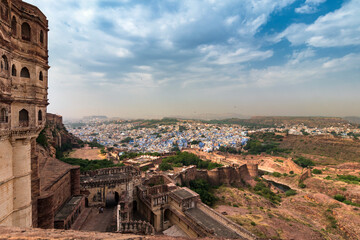 Obraz premium View of Mehrangarh fort with distant view of blue city Jodhpur, Rajasthan, India. Historical Fort is UNESCO world heritage site. Blue sky with white clouds in the background.