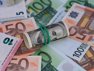 A tied stack of one hundred dollar bills lying on a euro bills background.