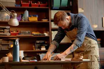Man working in well-organized workshop surrounded by tools and materials, crafting wooden projects with focused precision