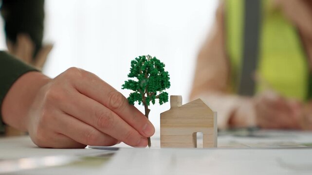 A video of architect using tree and home model to measure blueprint. Architect designing house construction on a table at studio, with architectural plan scattered around. Focus on hand. Delineation.