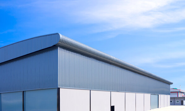 Large industrial warehouse building with roller shutter doors on concrete and corrugated aluminium wall in factory area against blue sky background, low angle and perspective side view