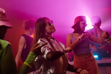 Side view of young brunette woman in trendy attire dancing among intercultural friends and enjoying...