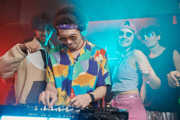 Young male deejay in headphones and stylish apparel bending over soundboard while standing in front...
