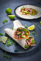 Italian style wrap piada wheat tortilla with tuna fish, vegetable and avocado served as closeup on a Nordic design plate