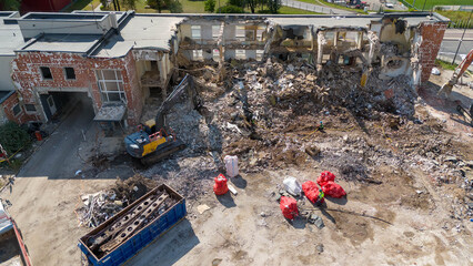 Drone photography of machinery dismantling a house and removing ruble during sunny summer day.