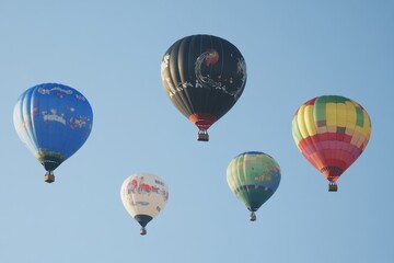 Naklejka premium colorful hot air balloons floating in the sky, each balloon adorned with unique designs and patterns. The balloons represent different colors such as blue, black, red, green, yellow, and purple.