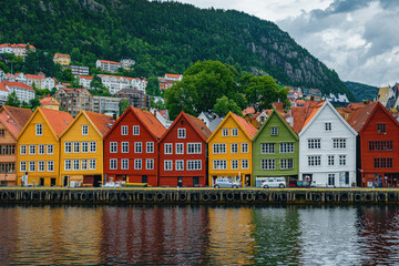 Fototapeta premium Colorful wooden houses line the historic Bryggen wharf in Bergen, Norway, reflecting beautifully on the calm waterfront with a hilly backdrop.