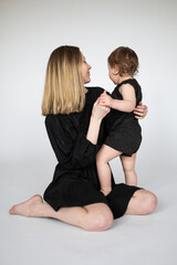 Glückliche junge blonde Mutter und Tochter in schwarzen Outfits isoliert auf weißem Hintergrund