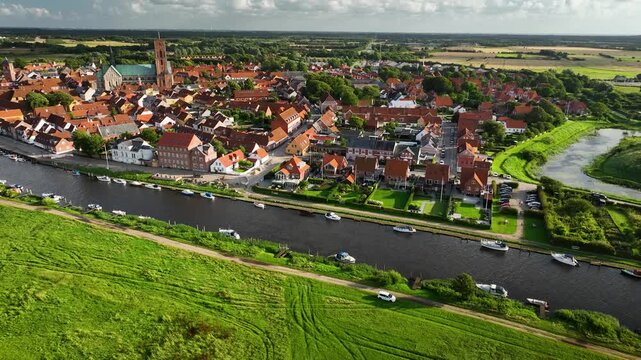 Aerial footage of historic town Ribe with majestic Ribe cathedral, red-roofed buildings and boats docked along the riverside, set against lush, green landscape, south-west Jutland, Denmark.