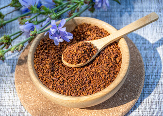 Ground chicory root on a wooden spoon and chicory flowers on a rustic wooden background. Alternative medicine. Healthy drinks. chicory drink