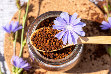 Ground chicory root on a wooden spoon and in a glass jar, chicory flowers on a rustic wooden background. Alternative medicine. Healthy drinks. chicory drink