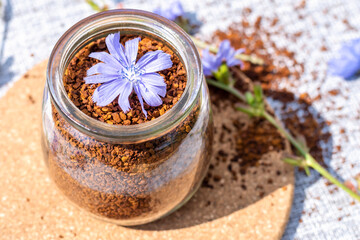 Ground chicory root in a glass jar and chicory flowers on a rustic wooden background. Alternative medicine. Healthy drinks. chicory drink