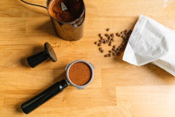 Top view of coffee grinder, ground coffee, and coffee beans on a wooden table.