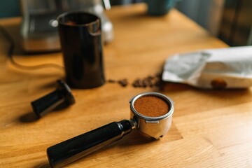 A portafilter filled with freshly ground coffee on a wooden countertop with a coffee grinder