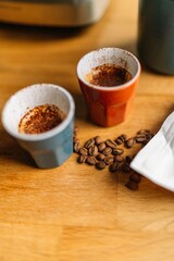 Two espresso cups with coffee beans on a wooden table