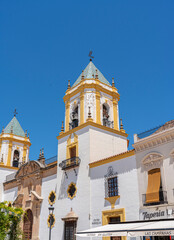 Fototapeta premium A close-up view of a historic church bell tower in Ronda, Spain, featuring classic yellow and white architectural details against a clear blue sky. Ideal for cultural and architectural themes.