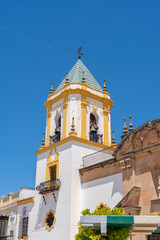 Fototapeta premium The stunning facade of the Church of Nuestra Señora de la Merced in Ronda, Spain, featuring twin bell towers and a central fountain under a bright blue sky. Perfect for themes of Spanish architecture