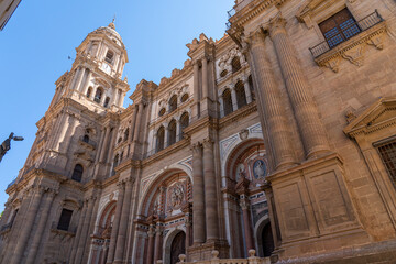 A striking view of the intricate facade of Málaga Cathedral, showcasing its grand architecture against a clear blue sky. Ideal for themes of historic landmarks, architecture, and Spanish heritage.