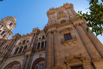 A striking view of the intricate facade of Málaga Cathedral, showcasing its grand architecture against a clear blue sky. Ideal for themes of historic landmarks, architecture, and Spanish heritage.
