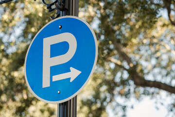 Round blue P for Parking sign with arrow, trees and sky in background