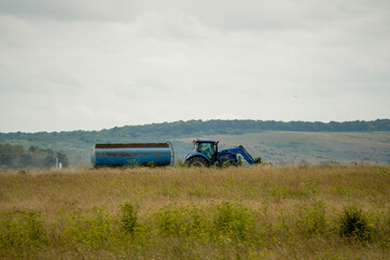 Fototapeta premium large blue New Hollnad T5 tractor towing a 30,000 litre water tanker in countryside