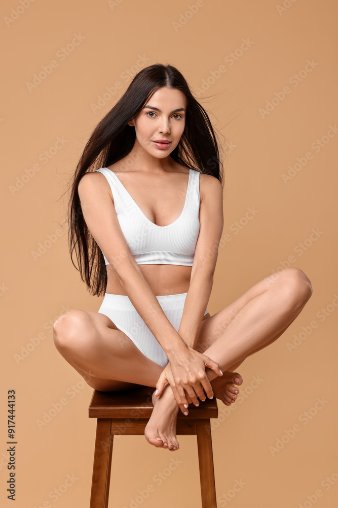 Poster Beautiful woman with perfect skin in underwear posing on stool against beige background. Body care